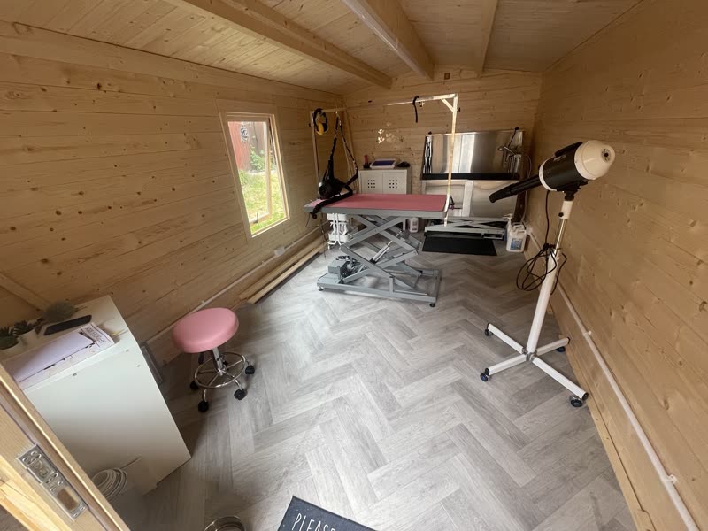 The timber-lined garden-room grooming studio with its pink grooming table, stool and lamp